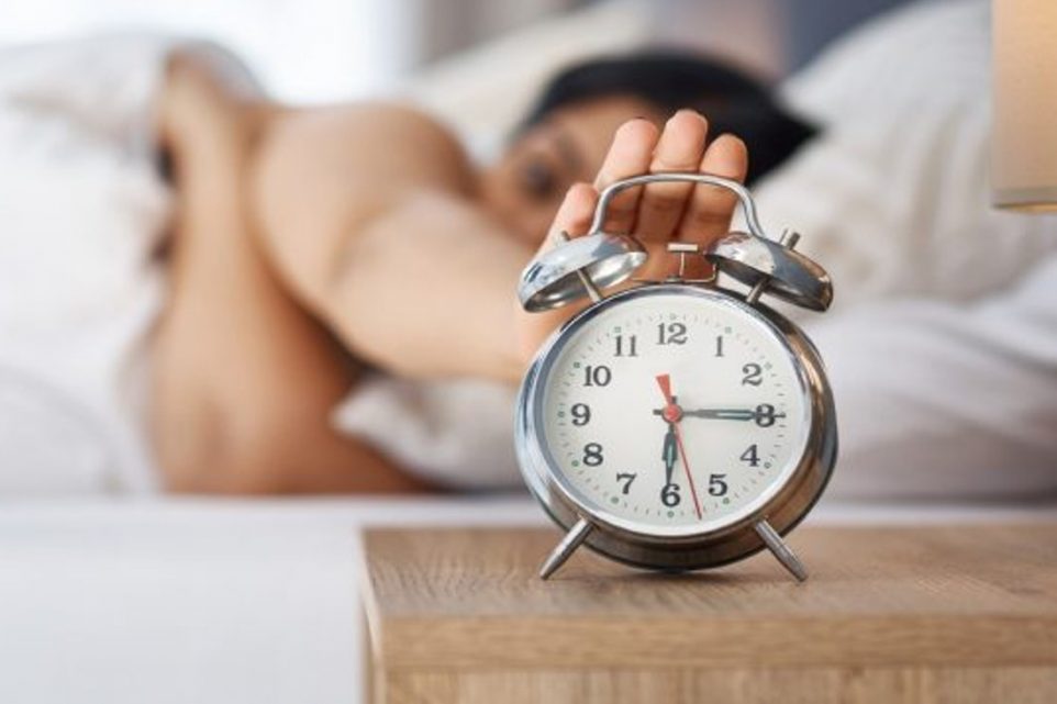 woman with her hand trying to reach the alarm clock
