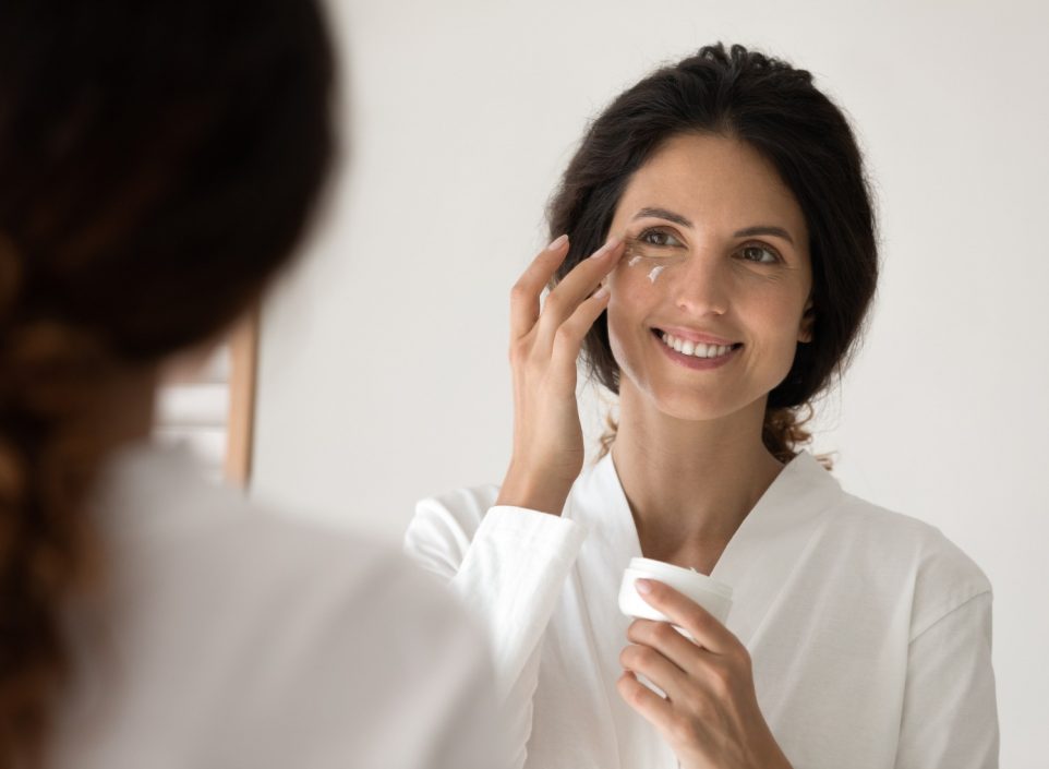 Woman applying eye cream in a mirror