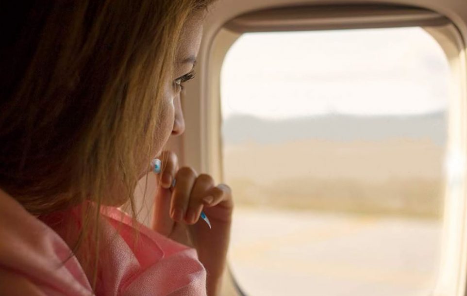 A lady looking out the window of a plane while using the Colgate Travel Toothbrush as she flies to her next destination.