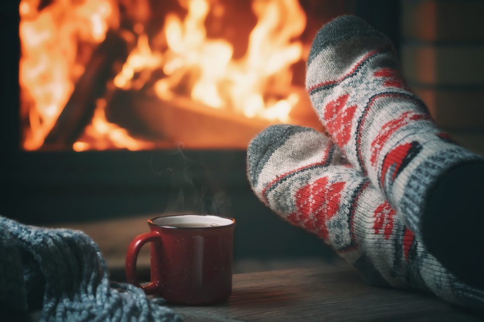 Girl resting and warming her feet by a burning fireplace in a country house on a winter evening. Selective focus