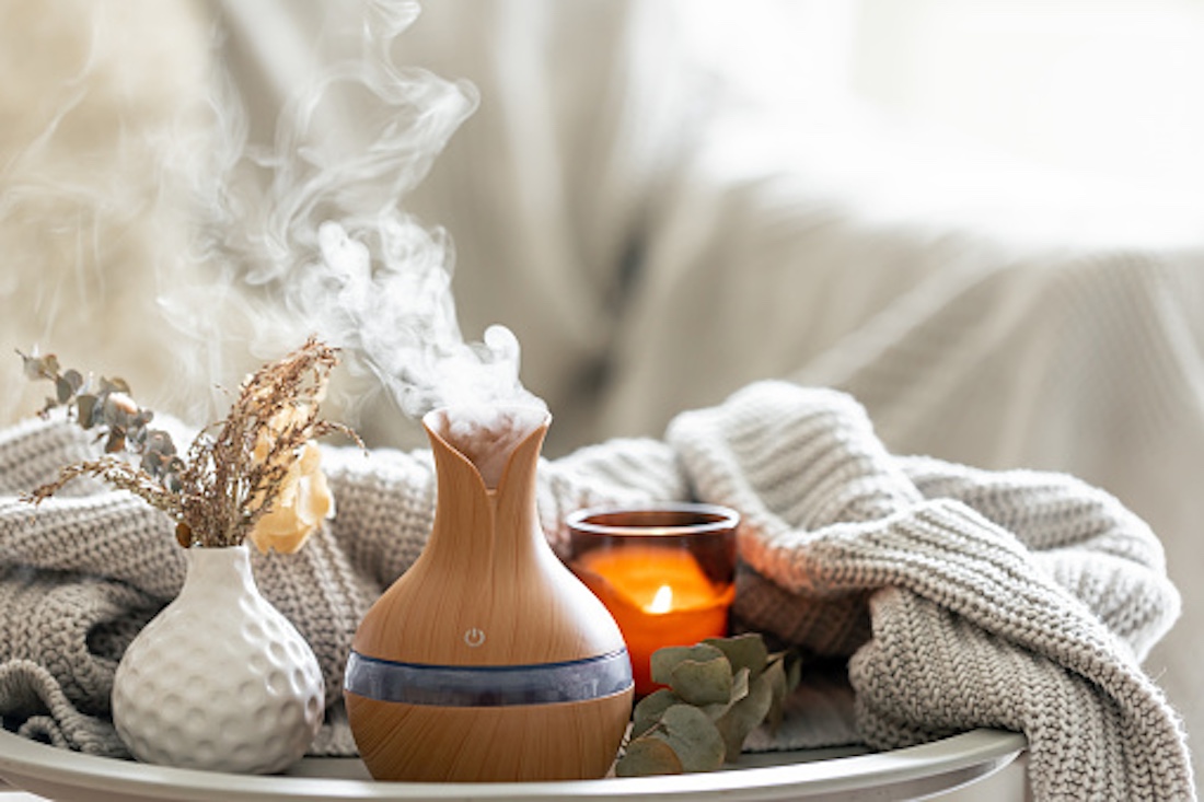 Aroma composition with a modern aroma oil diffuser, candles and a knitted element in interior of room. best aromatherapy diffuser