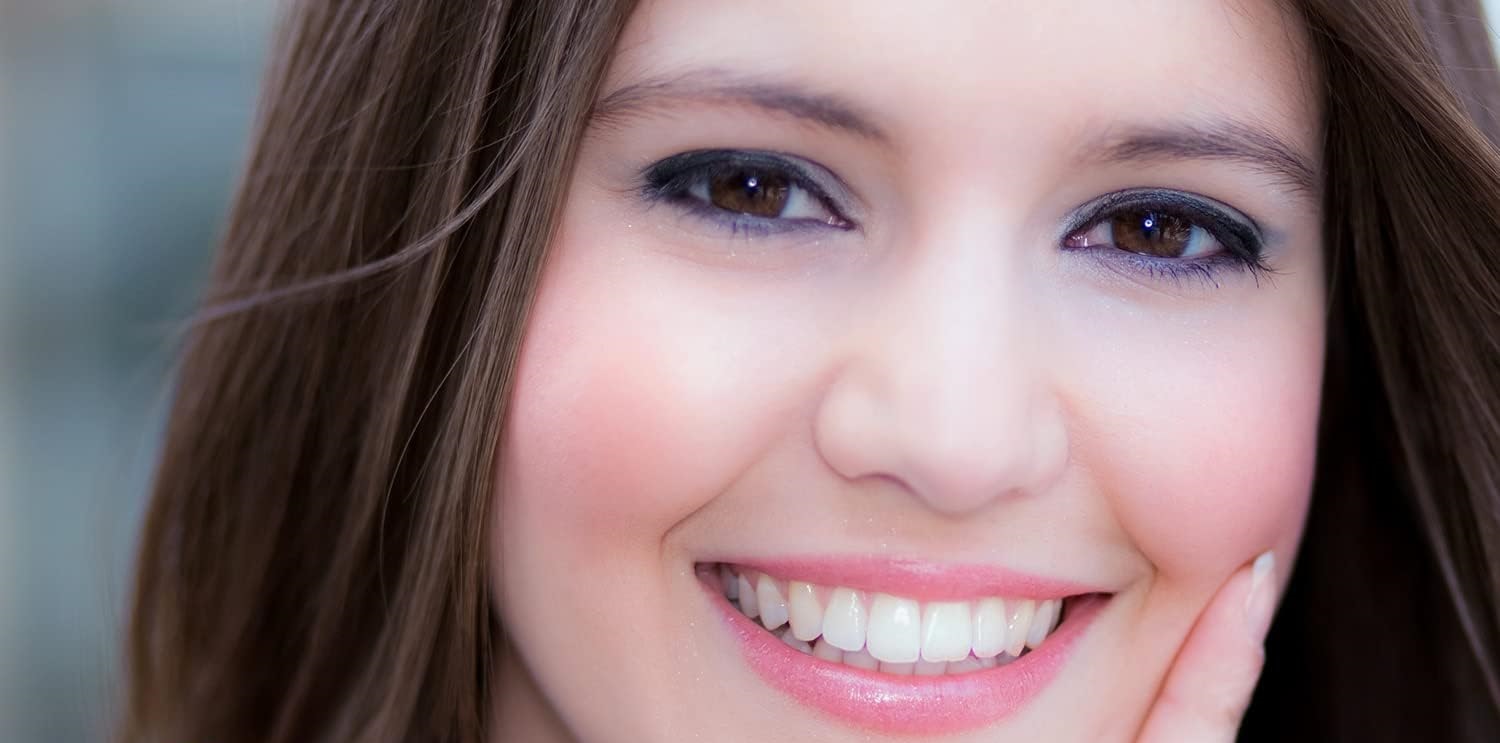 A young woman smiling confidently, showing off her bright, white teeth after using a tooth whitening kit.